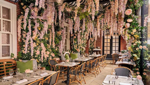 An outdoor dining area with tables and wicker chairs, surrounded by hanging floral arrangements. - The Bloomsbury (London)