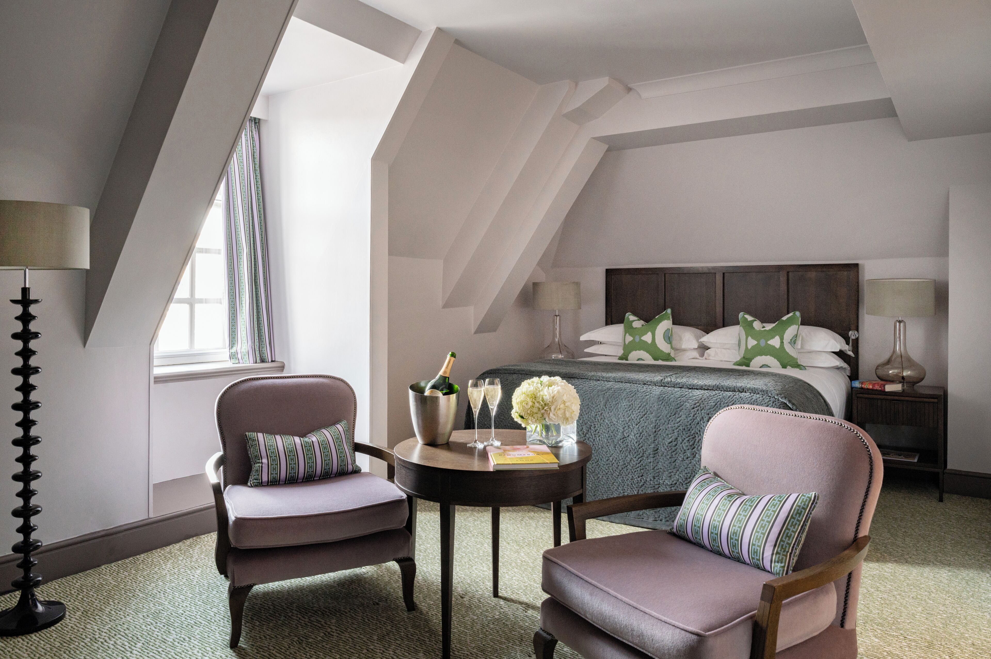 Ein Hotelzimmer mit einem großen Bett, zwei Sesseln, einem kleinen Tisch mit einer Champagnerflasche und einem Blumenstrauß.