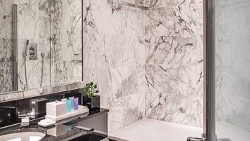 A modern bathroom with a marble wall, a large mirror, a black vanity, a bathtub, and a glass shower enclosure.