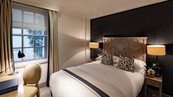 Une chambre d’hôtel avec un grand lit, deux lampes de chevet, un bureau avec une chaise et une fenêtre avec des rideaux.