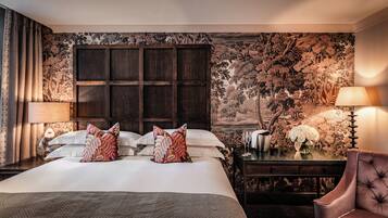 A hotel room with a large bed, two bedside tables with lamps, a chair, and a floral wallpaper.