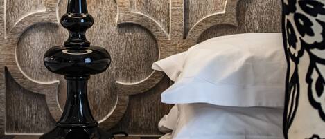 A neatly made bed with a white pillow and a black lamp on a wooden nightstand.
