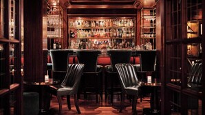 A bar area with wooden paneling, a well-stocked liquor shelf, and leather chairs. - The Bloomsbury (London)