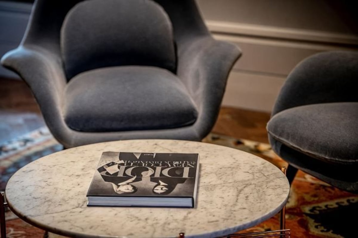 Una mesa redonda de mármol con un libro titulado 'Dior' y dos sillas grises tapizadas.
