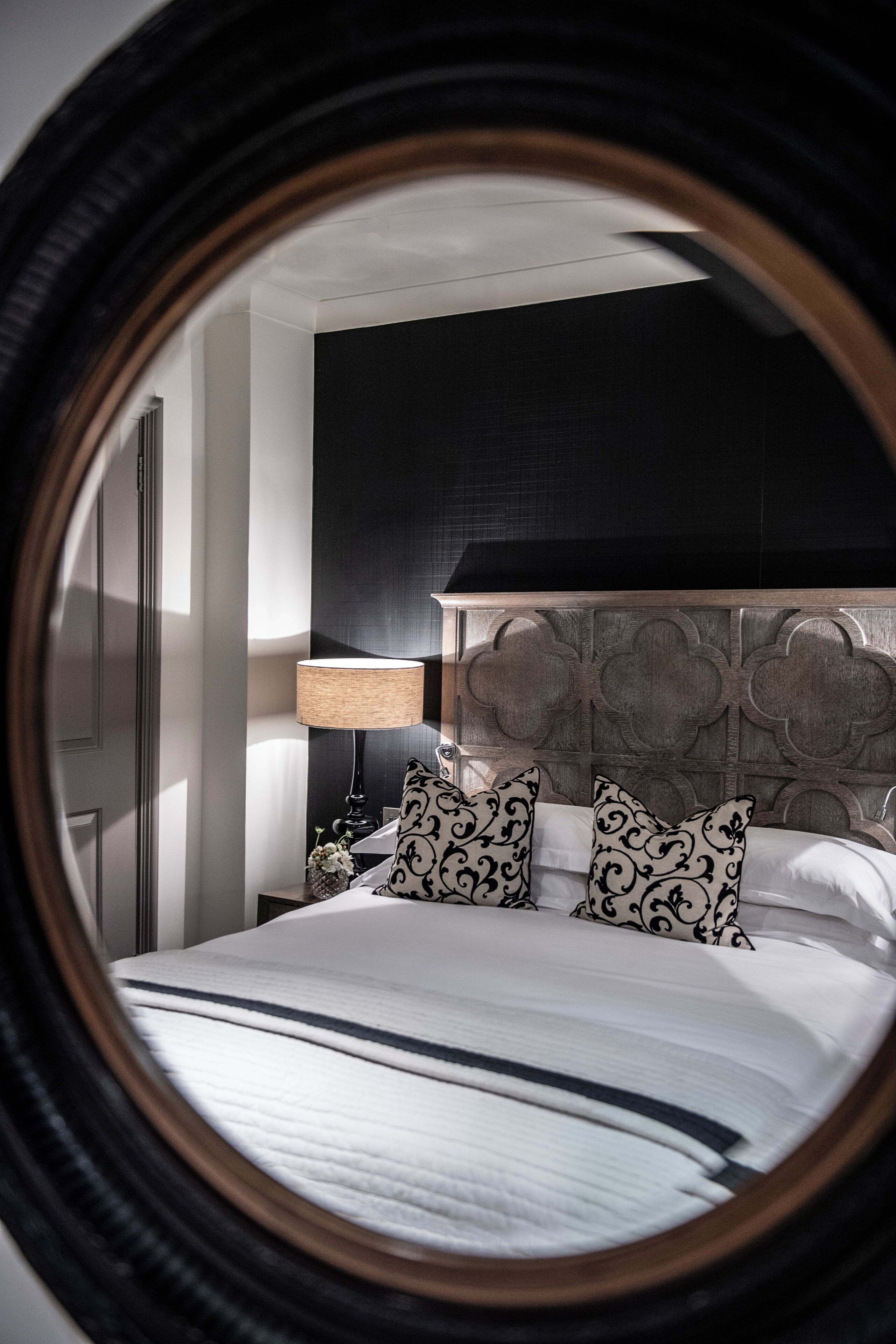 A bedroom with a large bed, a nightstand, a lamp, and a decorative headboard.
