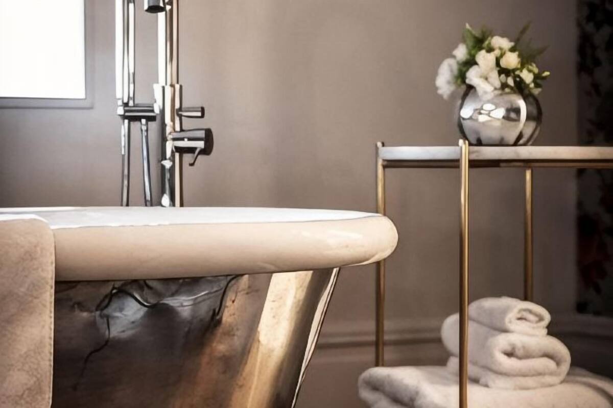 A bathroom with a marble sink, a gold-framed mirror, and a vase with flowers on a side table.