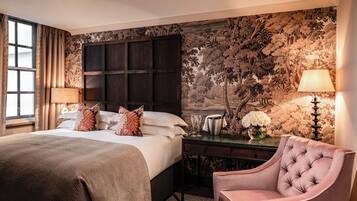 A hotel room with a large bed, a nightstand with a lamp, a chair, and a wall with a floral mural.