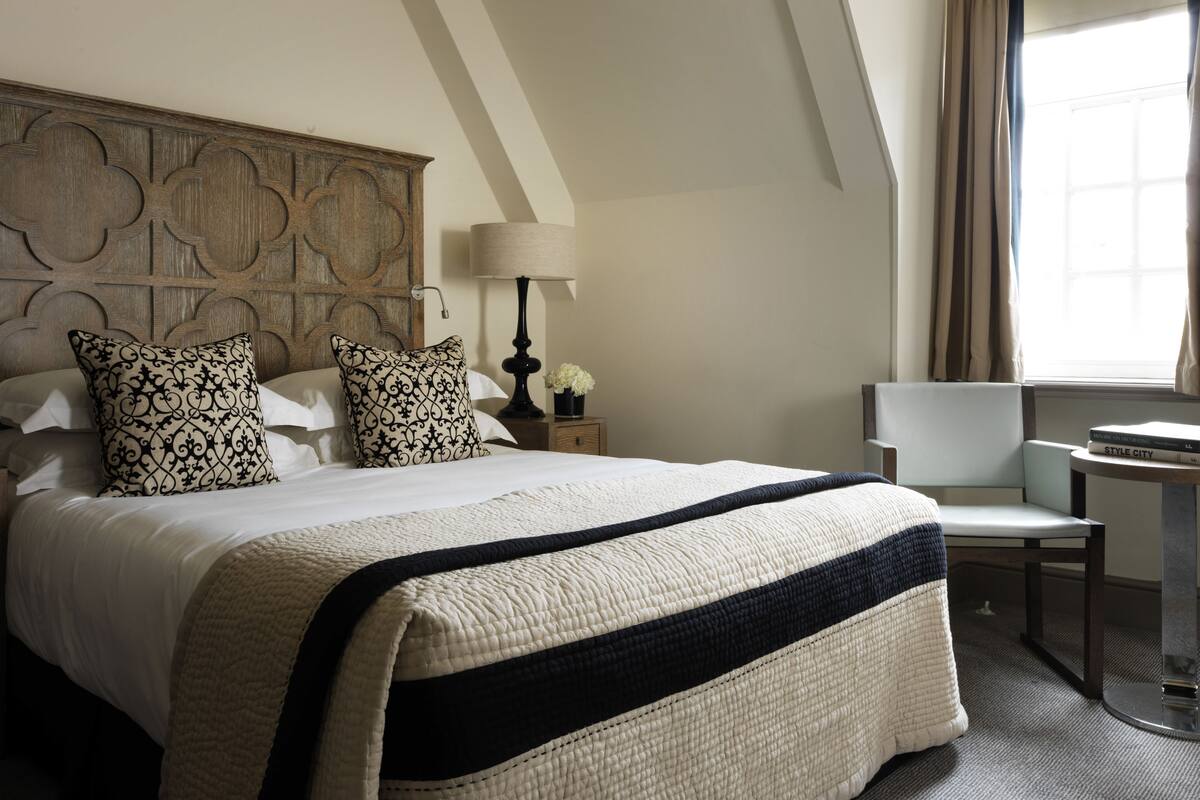 A hotel room with a large bed, a nightstand with a lamp, a chair, and a small table.