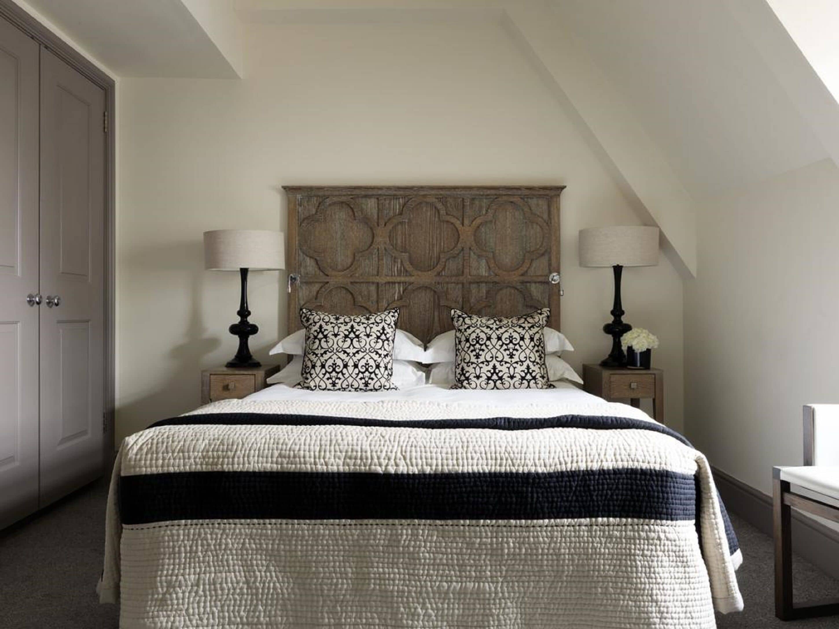 A bedroom with a large bed, two bedside tables with lamps, a wooden headboard, and a door.