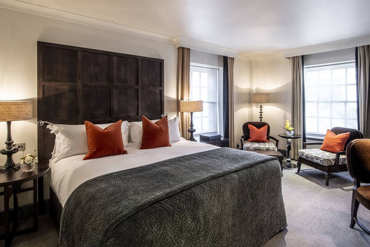 A hotel room with a large bed, two bedside tables, a desk, a chair, and a window with curtains.