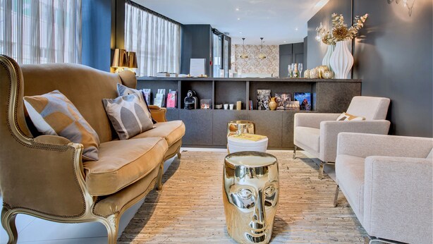 A modern living room with a brown sofa, a white armchair, and a unique glass coffee table. - Villa des Ambassadeurs (Paris)
