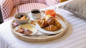 A breakfast tray with croissants, cheese, ham, and a glass of orange juice on a bed with striped bedding. - Villa des Ambassadeurs (Paris)