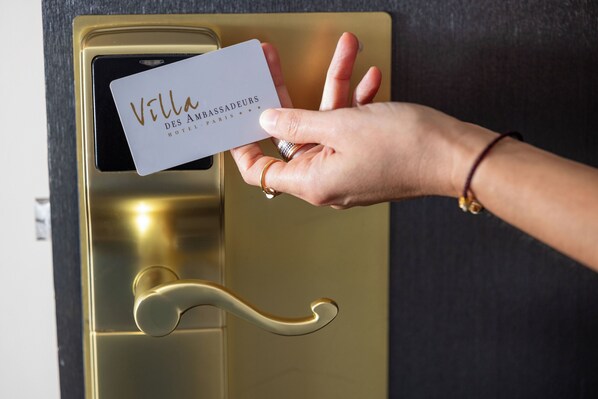 Una mano sostiene una tarjeta con la inscripción 'Villa Des Ambassadeurs HOTEL PARIS', frente a un pomo dorado.
