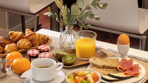A breakfast setup with croissants, fruits, eggs, and juice on a table. - Villa des Ambassadeurs (Paris)