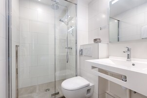 A modern bathroom with a glass-enclosed shower, a white toilet, and a white sink with a mirror above it.