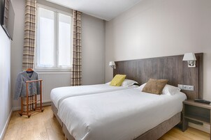 A hotel room with two beds, a wooden nightstand, a lamp, and a window with curtains.