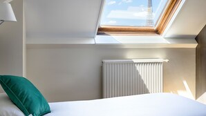 A hotel room with a skylight, a bed with a green pillow, a white radiator, and a view of the Eiffel Tower. - Beaugency Hotel (Paris)
