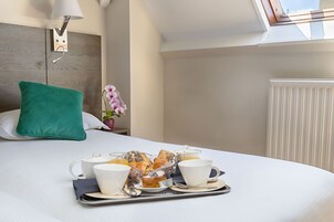 A neatly made bed with a tray of breakfast items, including pastries, coffee cups, and a teapot.
