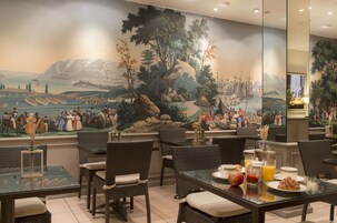 A dining area with wicker chairs and tables, a mural depicting a historical scene, and breakfast items on the tables.