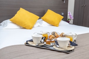 A neatly arranged breakfast tray on a bed with a white bedspread, two yellow pillows, and a small potted orchid in the background.