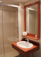 A bathroom with a glass shower enclosure, a white sink with a wooden countertop, and a mirror above the sink.