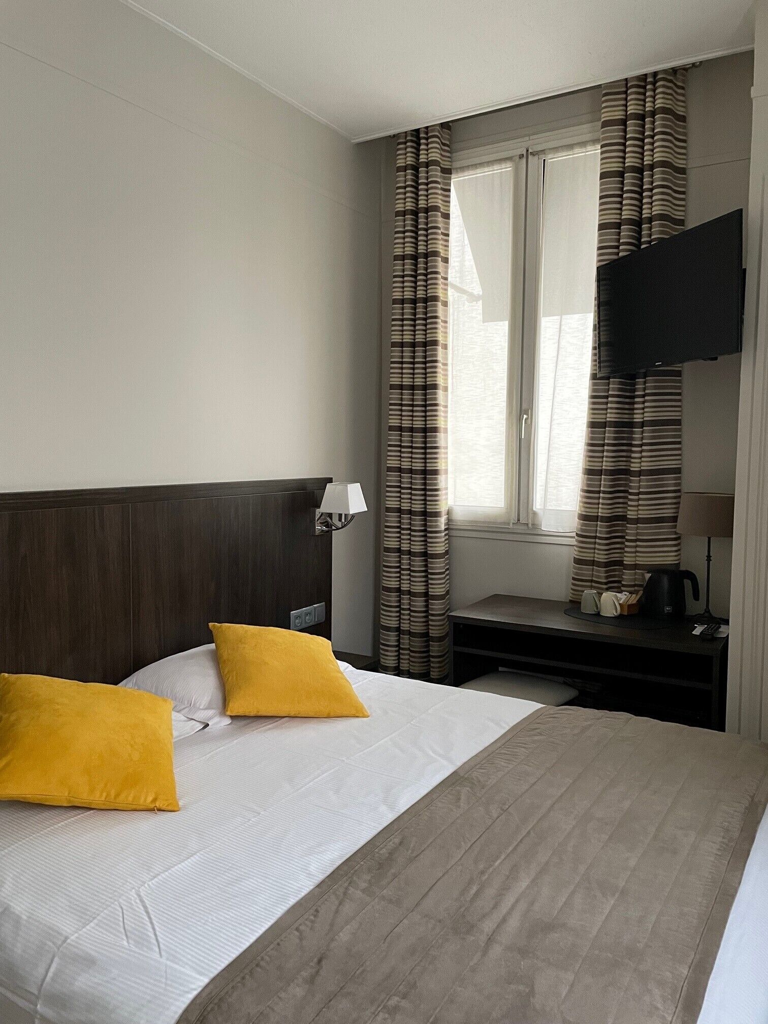 A hotel room with a bed, a desk, a television, and curtains.