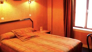 A hotel room with a bed, two wall-mounted lamps, a window with curtains, and a picture on the wall.