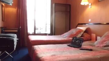 A hotel room with two beds, a desk, a chair, a TV, and a window.
