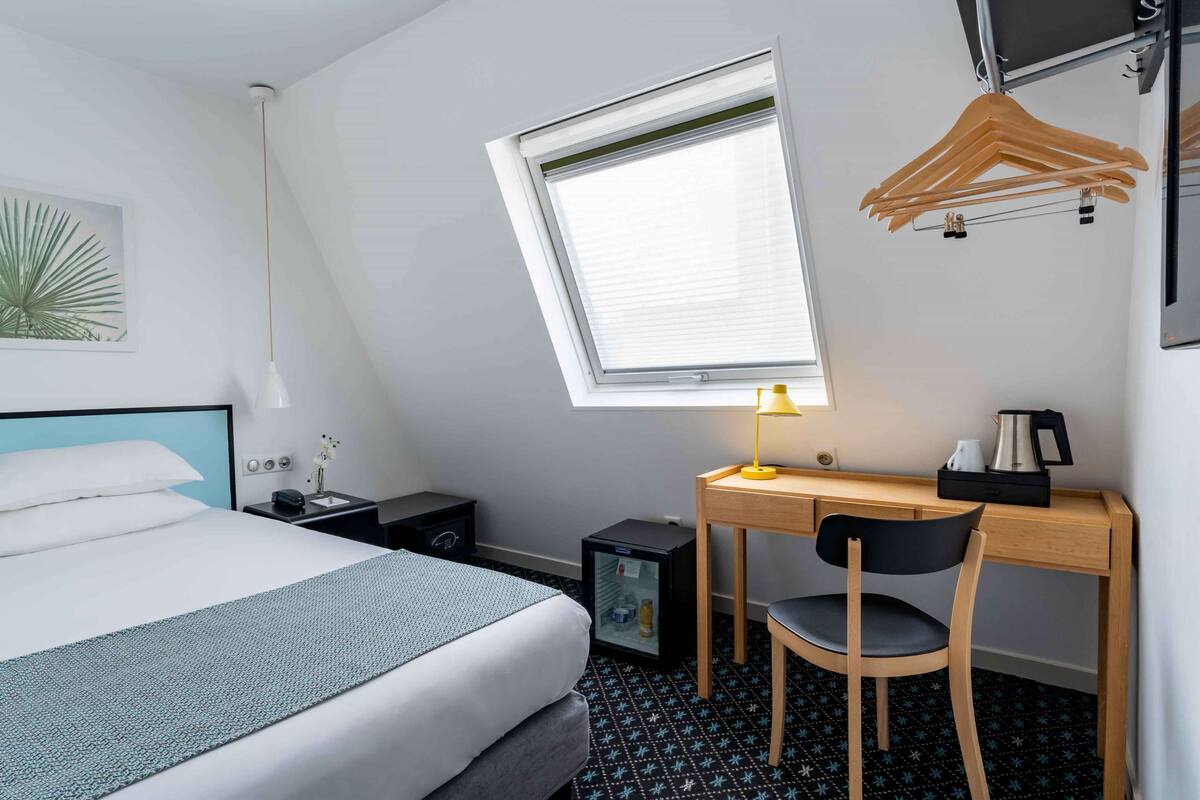 A hotel room with a bed, desk, chair, and a small refrigerator.