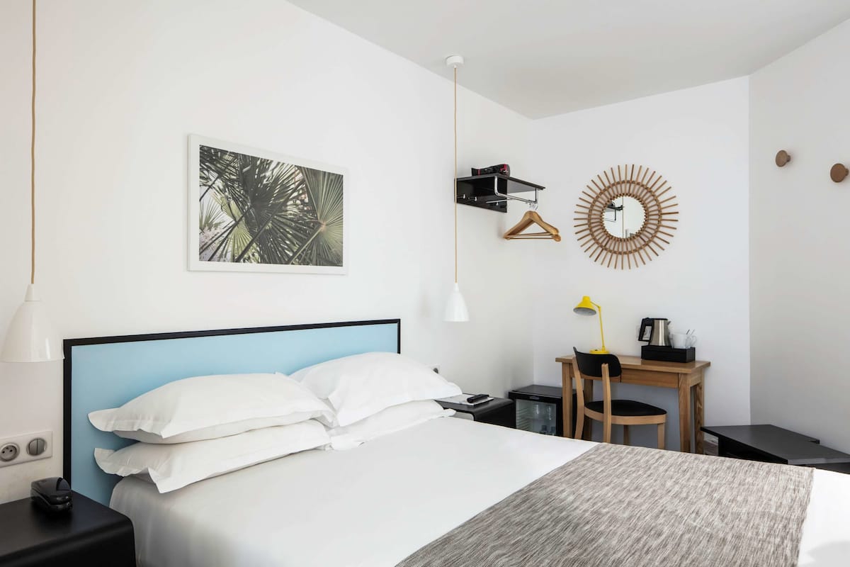 A neatly arranged hotel room with a bed, bedside table, desk, and chair.