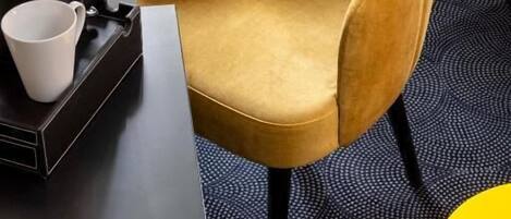 Una stanza con una poltrona giallo senape, un tavolino nero con una tazza bianca e un comodino giallo.