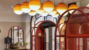 A modern interior with multiple orange spherical pendant lights, a mirrored wall, and red metal partitions. - Hotel Régina Opéra Grands Boulevards (Paris)