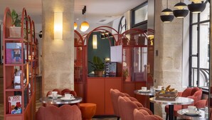 A modern dining area with red chairs, round tables, and a red bookshelf. - Hotel Régina Opéra Grands Boulevards (Paris)