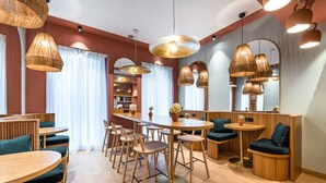 A modern dining area with wooden tables and chairs, a central round table, and hanging pendant lights. - O.lysée Hôtel (Paris)