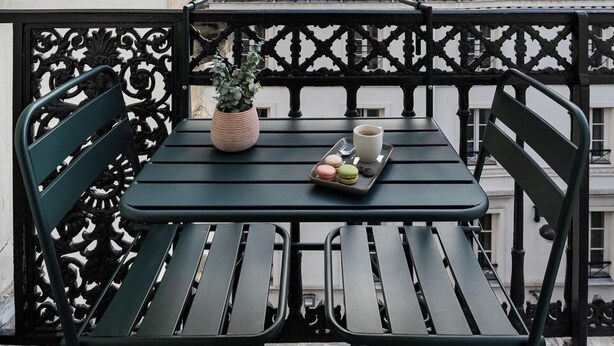 A balcony with a table and chairs, a potted plant, and a tray with food and drinks. - O.lysée Hôtel (Paris)