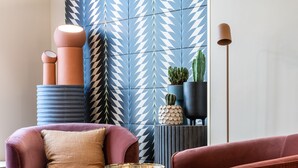 A modern living room with a patterned wall, a red sofa, a small table, and a floor lamp. - O.lysée Hôtel (Paris)