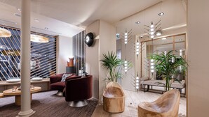 A modern living room with a red sofa, wooden coffee table, and a large potted plant. - O.lysée Hôtel (Paris)