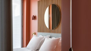 A bedroom with a bed, pillows, a wall-mounted mirror, and a wooden panel design. - O.lysée Hôtel (Paris)