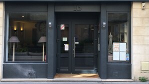 Exterior del Hotel Du Maine con un letrero grande sobre la entrada, una puerta con ventanal y una pequeña estatua en el exterior.