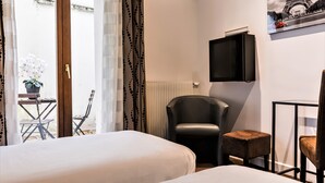 Habitación de hotel con dos camas, un sillón de cuero negro, un taburete pequeño, un televisor y vistas a la Torre Eiffel a través de una ventana.