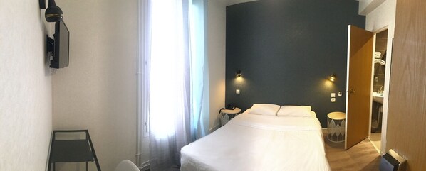 A hotel room with a bed, a desk, a chair, a wardrobe, and a bathroom visible through an open door. - Hôtel du Maine (Paris)