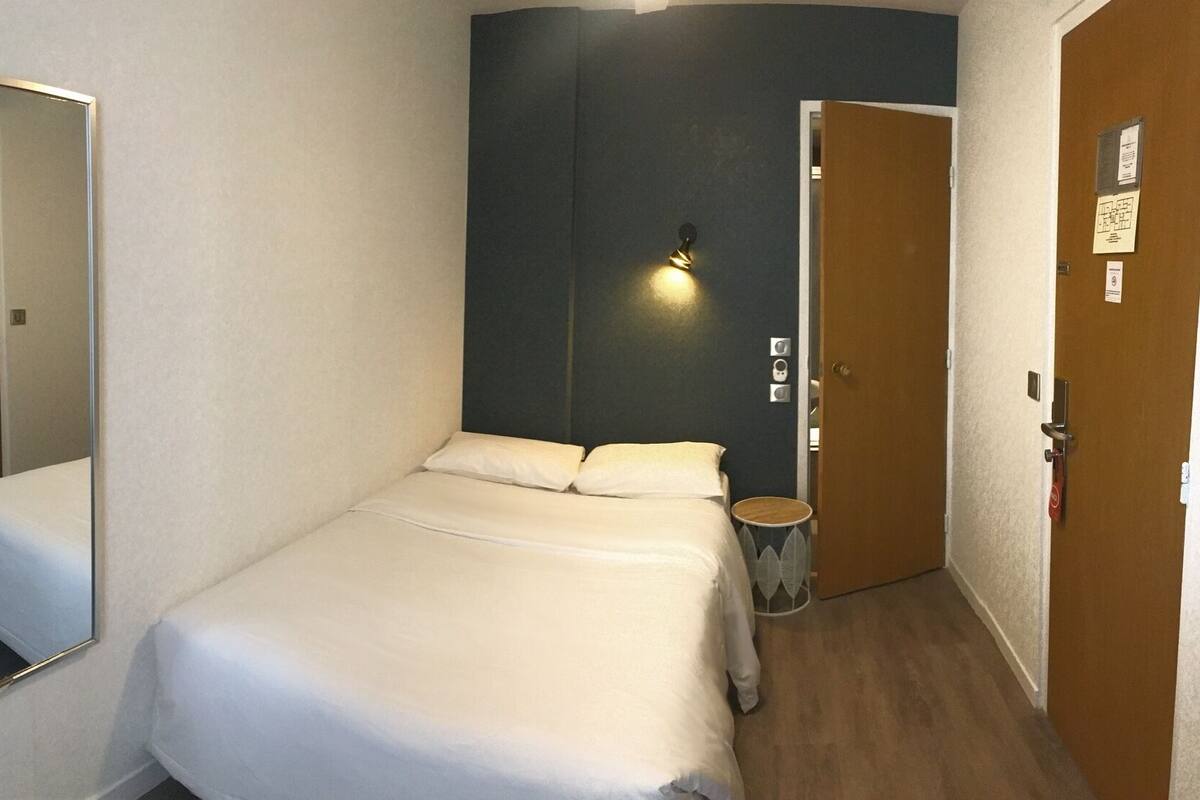 A single bed with white bedding in a room with a dark accent wall and a door with a light switch.