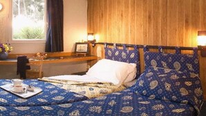 A hotel room with a wooden headboard, a bed with patterned bedding, a bedside table with a lamp, and a window with curtains. - Stars Antibes (Antibes)