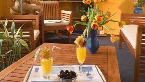 A wooden table with a tray of drinks and a bowl of olives, surrounded by chairs and a bookshelf with nautical decorations. - Stars Antibes (Antibes)