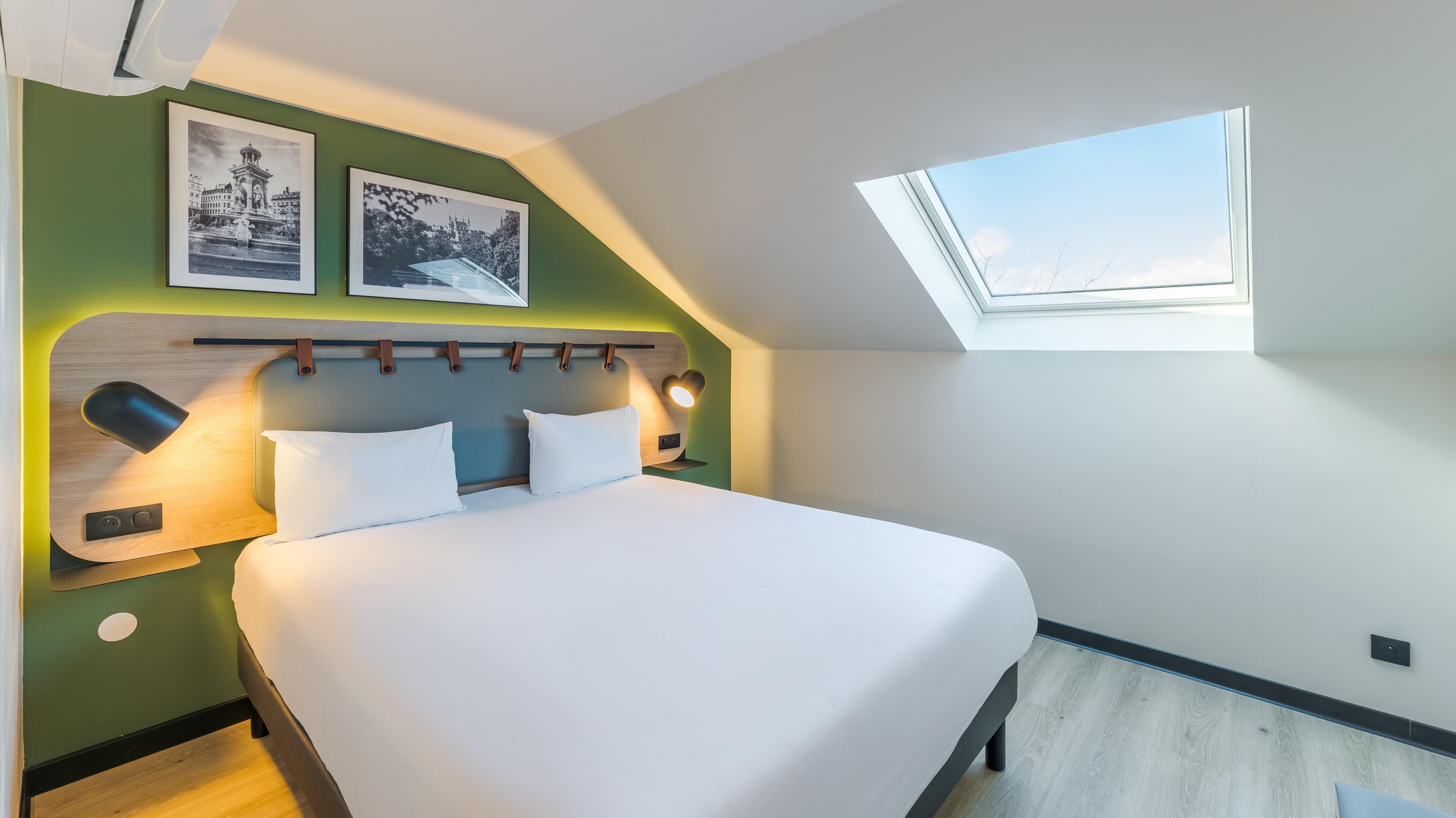 A modern bedroom with a large bed, a skylight, and two framed pictures on the wall.