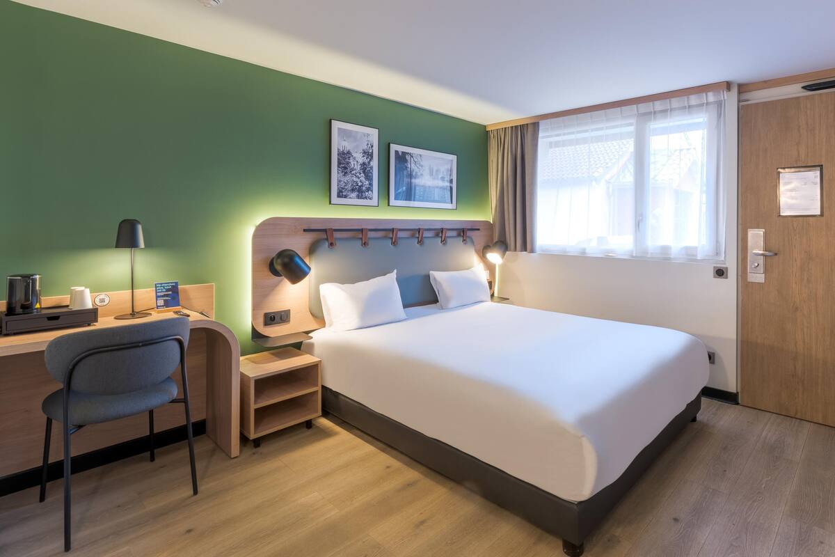 Een hotelkamer met een bed, een bureau, een stoel, een nachtkastje en een raam met gordijnen.