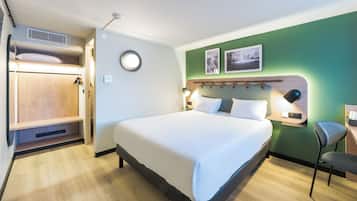 Une chambre d’hôtel comprenant un lit, une armoire, un bureau et deux cadres photos fixés au mur.