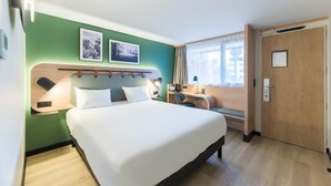 Une chambre d’hôtel avec un grand lit, un bureau, une chaise et deux tableaux encadrés au mur.