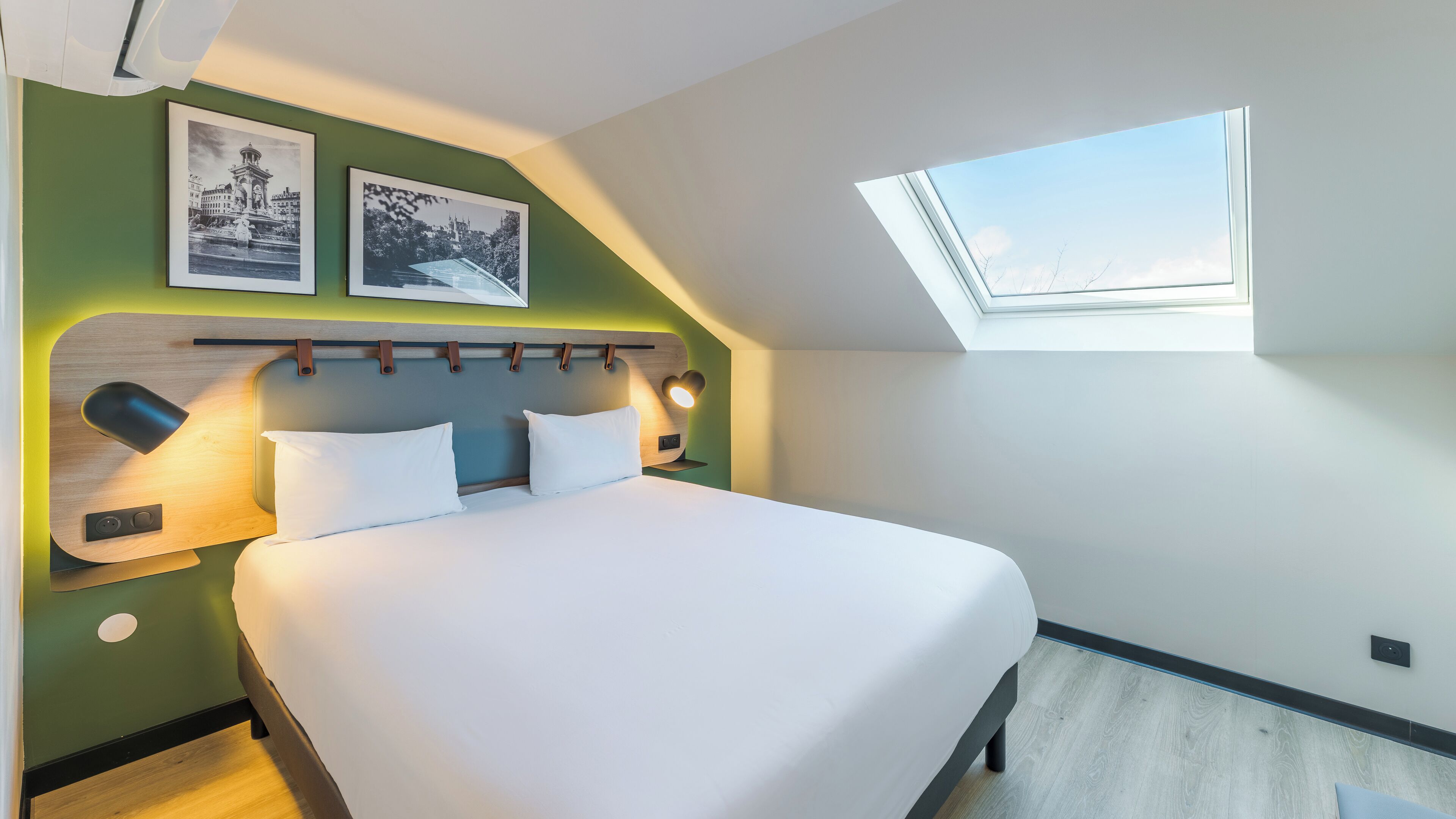 A modern bedroom with a large bed, a skylight, and two framed pictures on the wall.