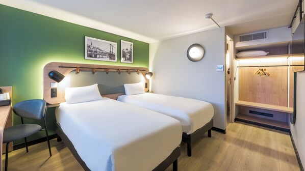 A hotel room with two beds, a desk, a chair, a clock, and a coat rack.